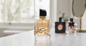A close-up of a YSL Libre Eau de Parfum bottle with its signature gold logo, set against a blurred, light-filled window.