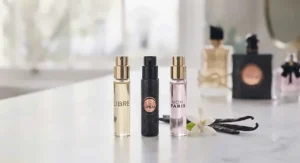 Three travel-sized YSL perfume atomisers lined up on a table, accompanied by vanilla beans and a white floral accent.