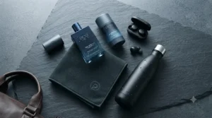 A premium men's grooming kit flat lay featuring a post-workout fragrance, deodorant, microfiber gym towel, and water bottle on a dark slate surface.